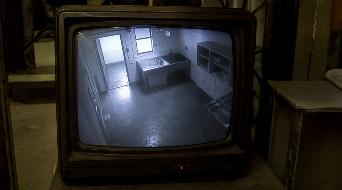 Grainy CCTV monitor view of an empty laundromat utility room.