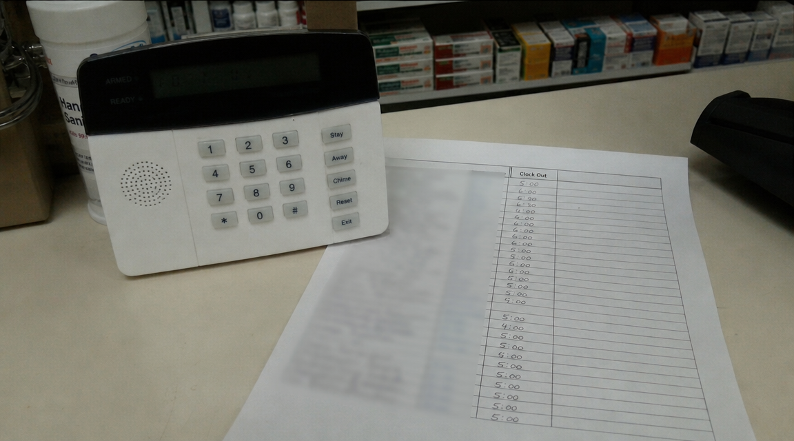 Close-up of a pharmacy alarm keypad beside an employee clock-out sheet after closing.