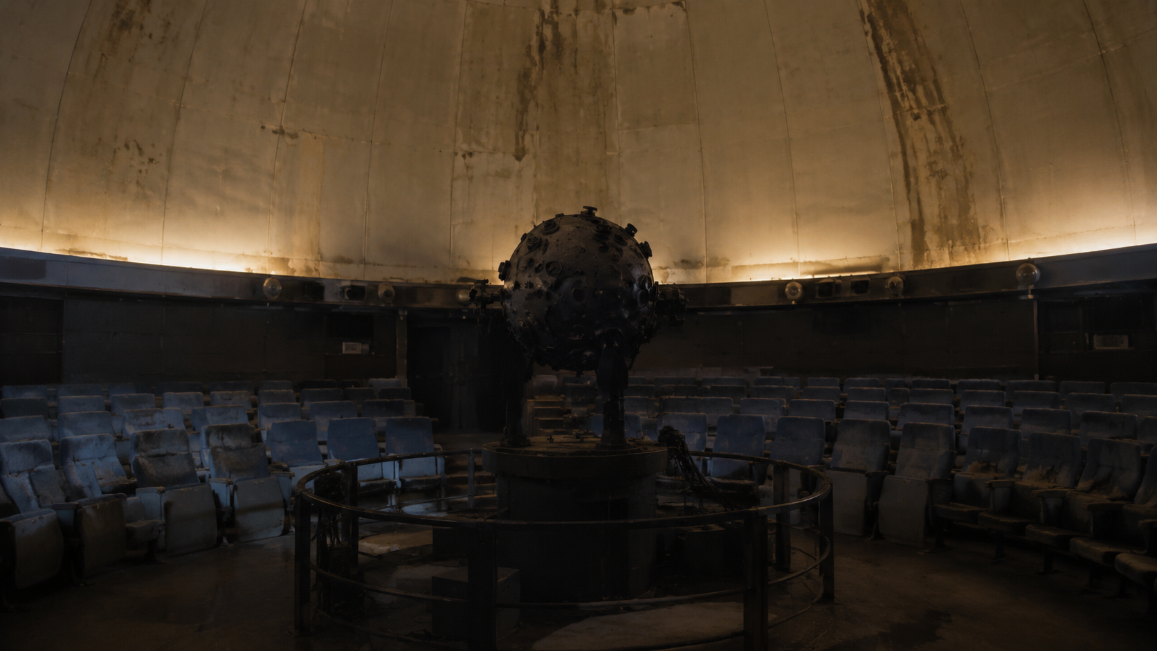 An abandoned planetarium theater with a star projector facing dusty blue seats beneath a stained dome.