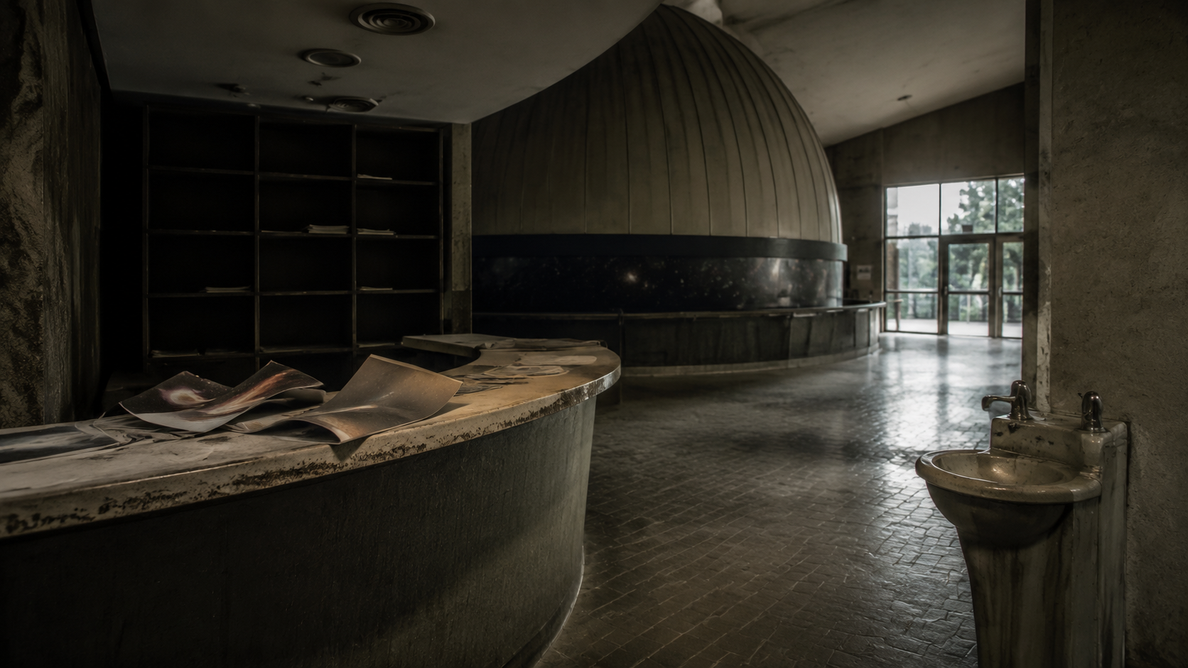 A closed planetarium lobby with abandoned brochures, an empty rack, and dim light through dirty doors.