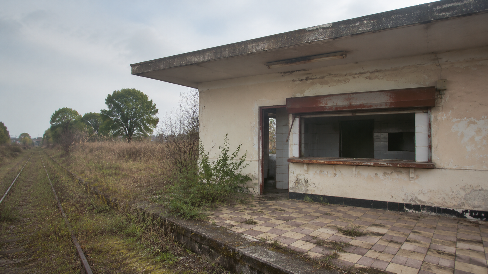 The ruined remains of a railway canteen beside old tracks under grey light.