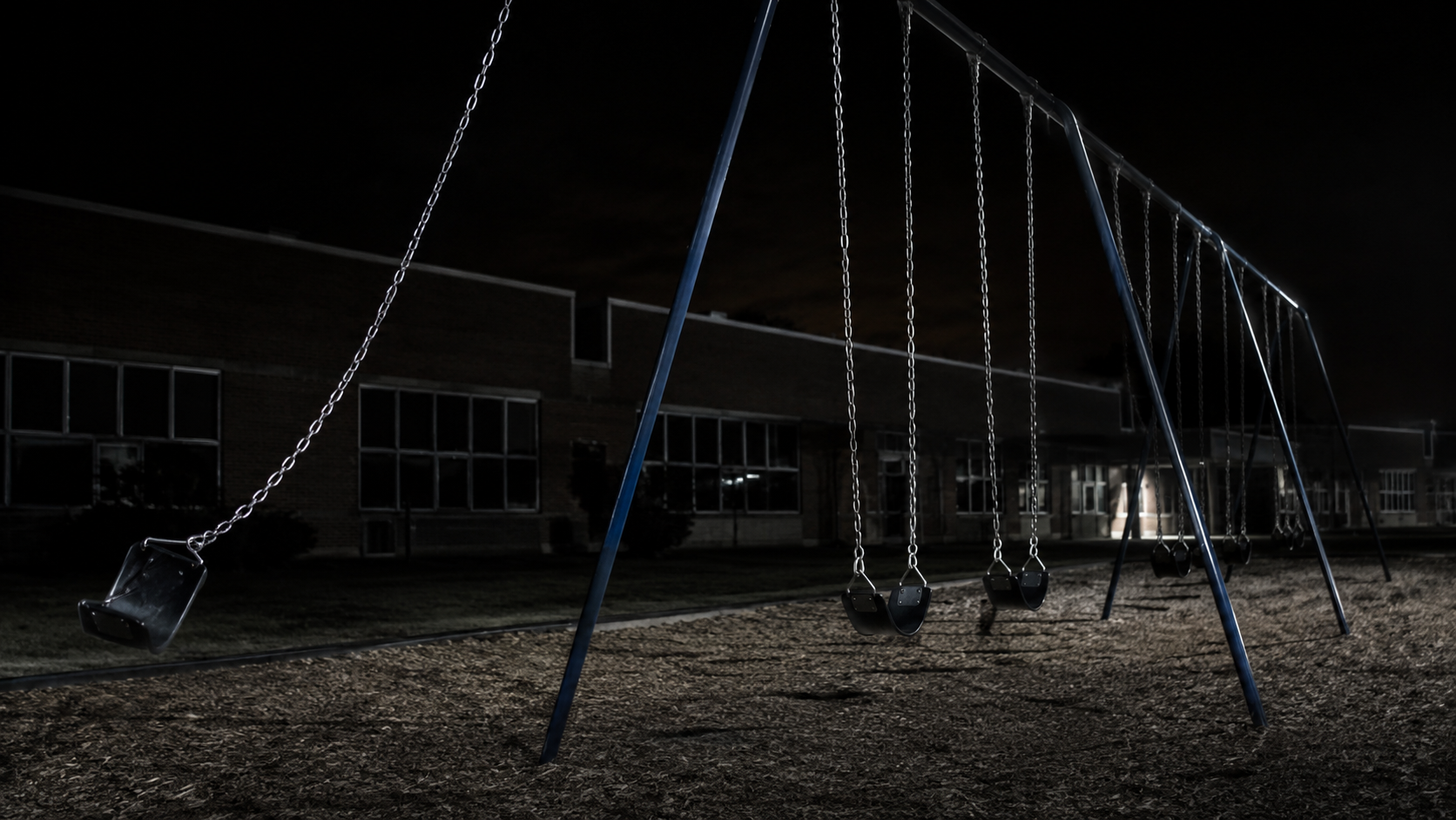 A still playground swing set with one chain stretched sideways in the dark.