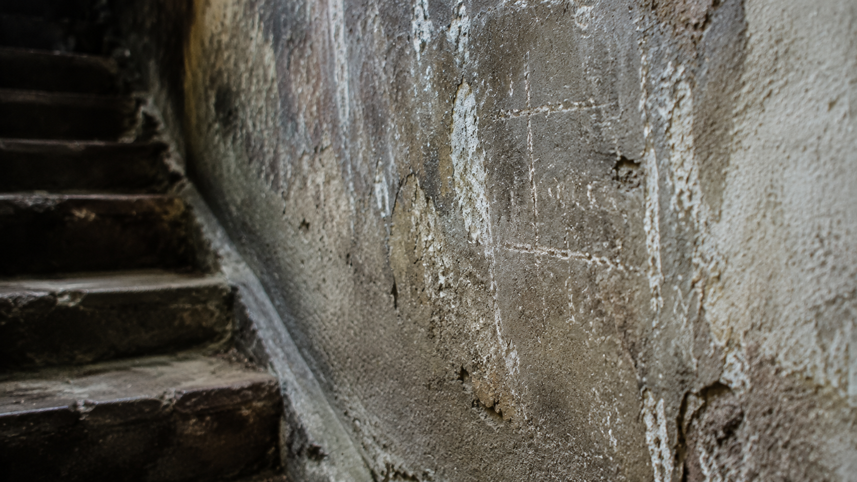Faint chalk marks on a damp cellar wall beside worn stone steps.