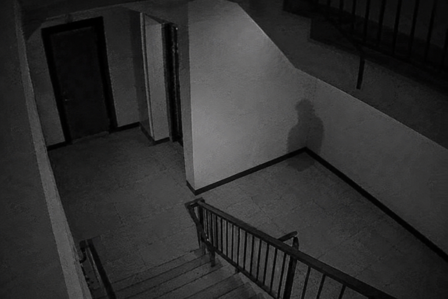 Security camera view of dark human-shaped shadow on stairwell landing