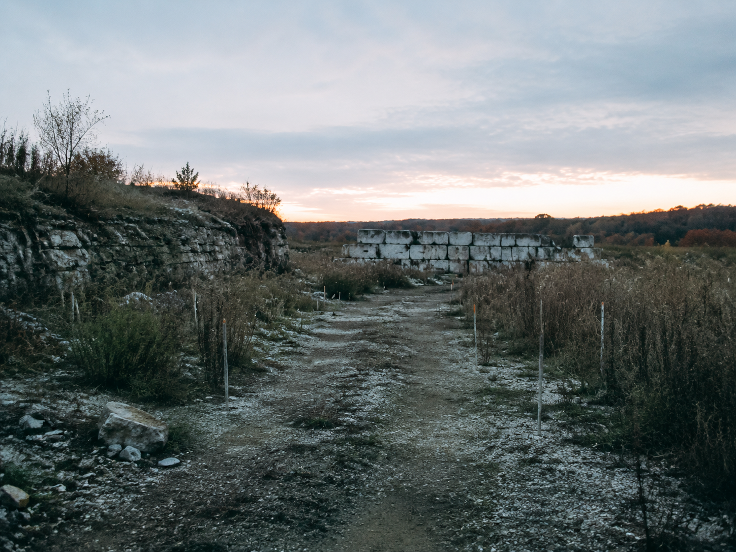 Abandoned quarry access road with survey stakes and limestone blocks at dusk
