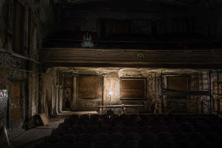 A long-haired apparition in a white dress sits alone in the balcony of a boarded-up theater under renovation.