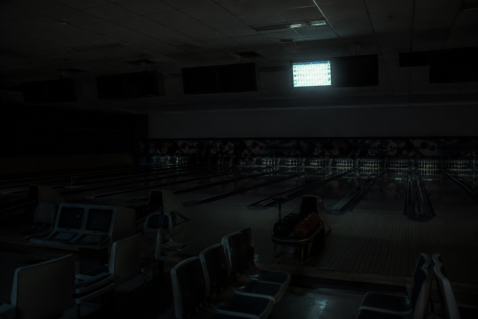 Empty bowling alley after closing with one overhead scoreboard glowing above a dark lane.