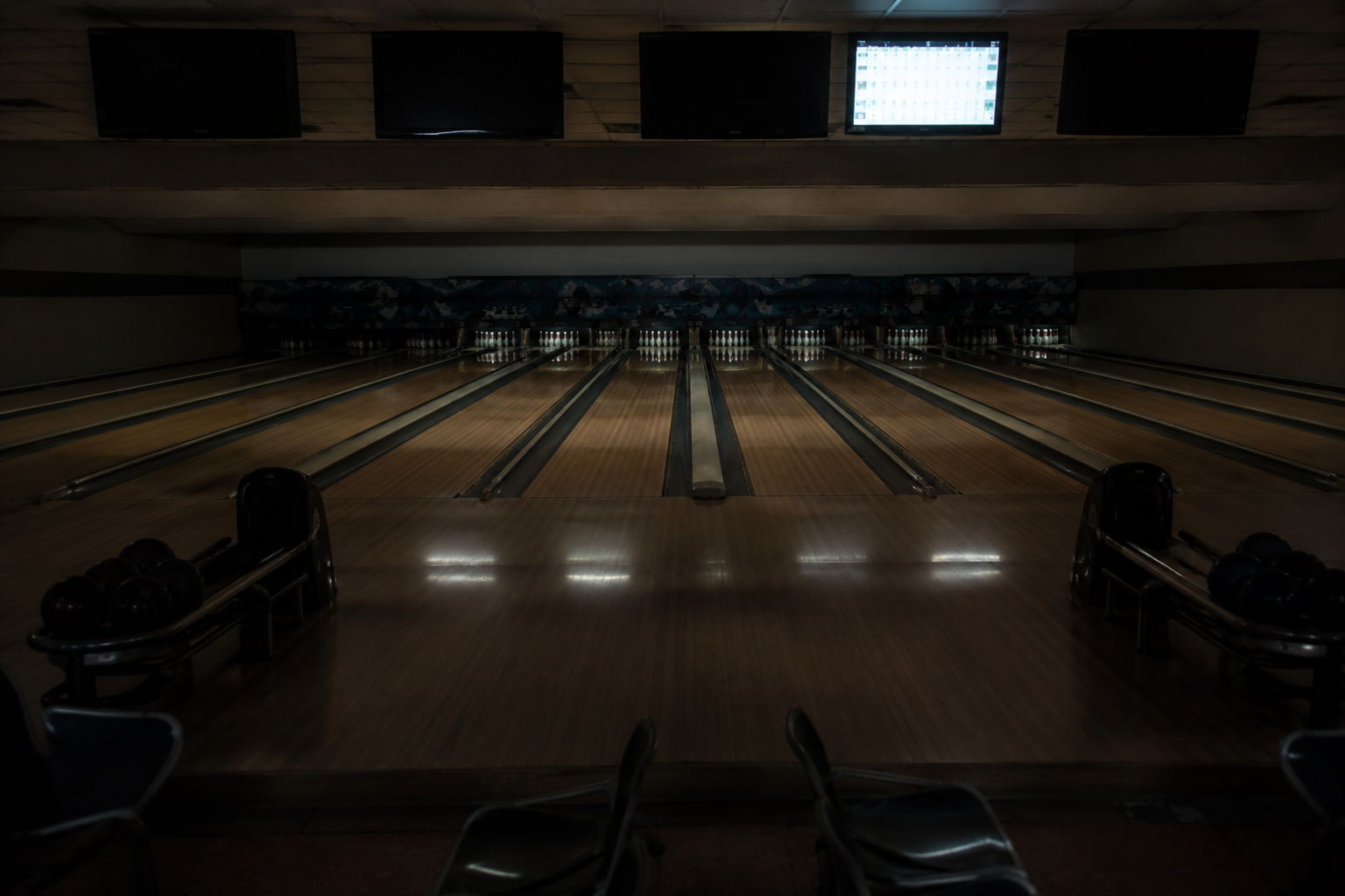 Security camera view of deserted bowling lanes with a single scoreboard lit after hours.