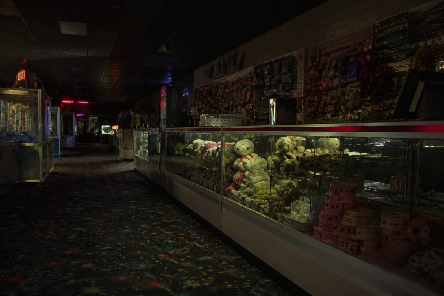 Closed arcade prize counter after hours with glass cases and dim neon reflections