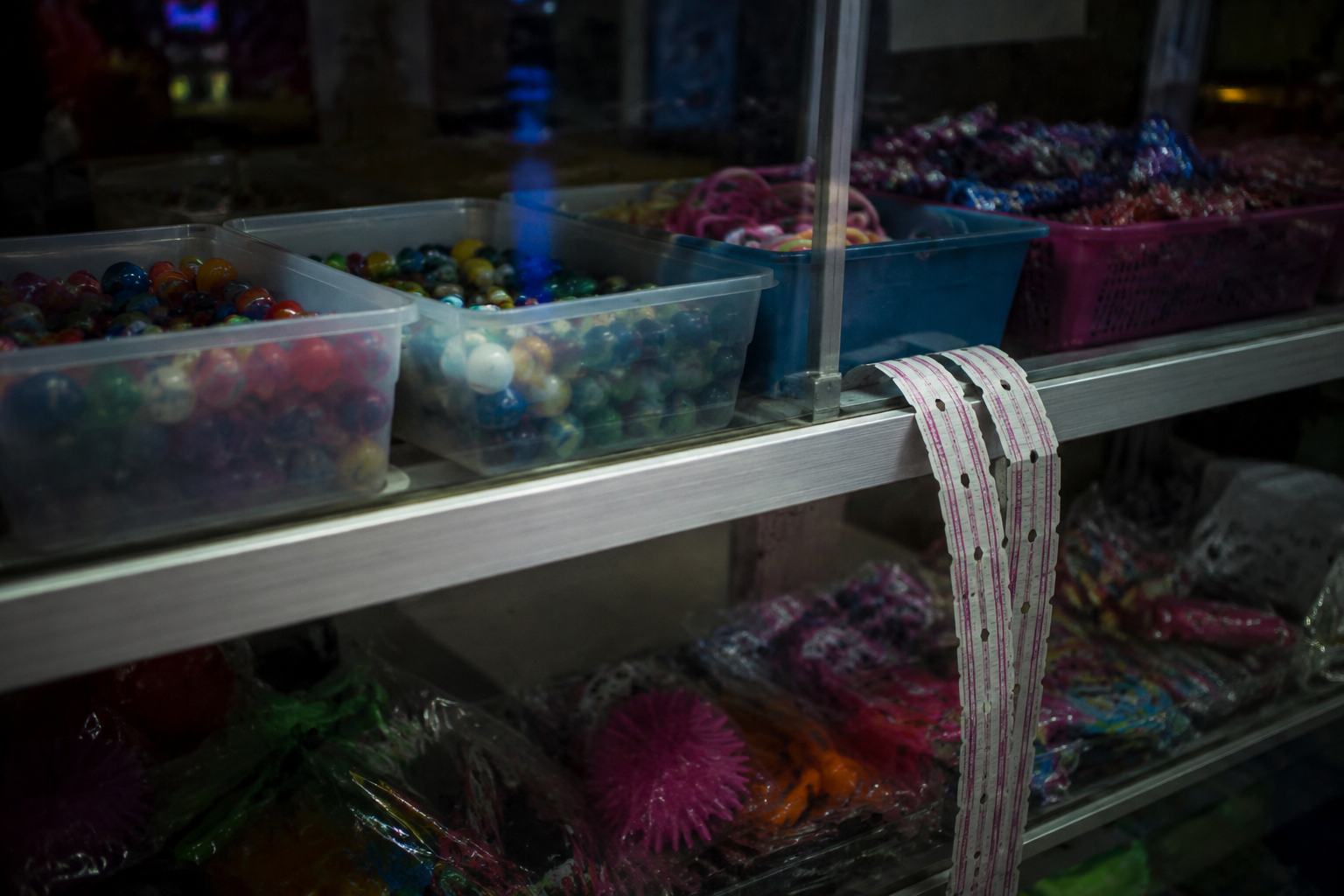 Prize counter glass case with toys and a ticket strip hanging over the edge