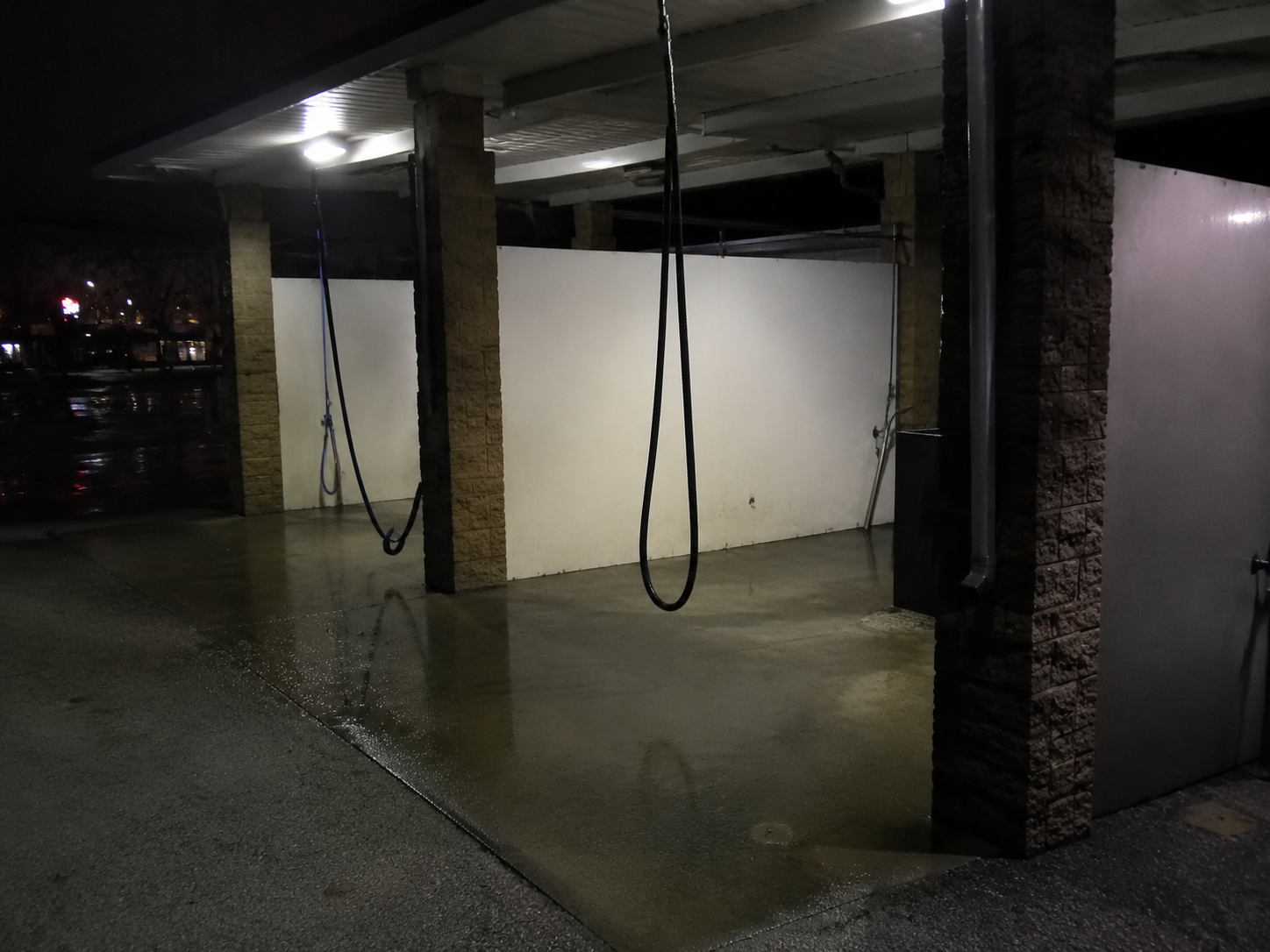 A vacuum hose hangs in a closed car wash bay over wet concrete at night.