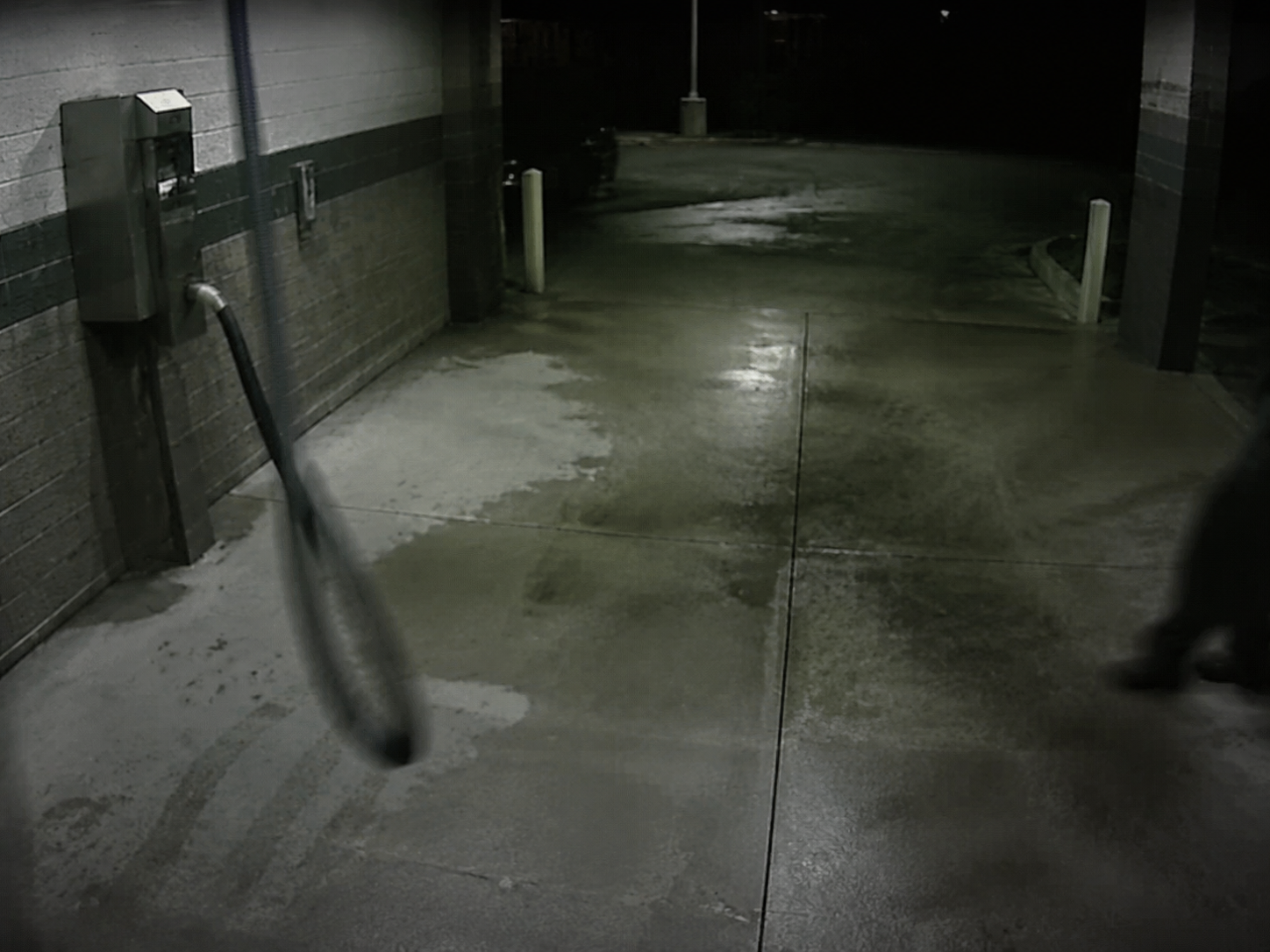 A second shadow crosses the wet concrete near a swinging vacuum hose.