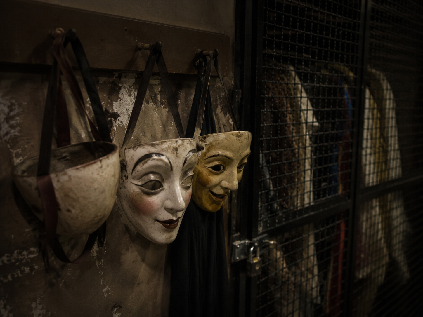 Theater masks on hooks with one mask turned toward the wall