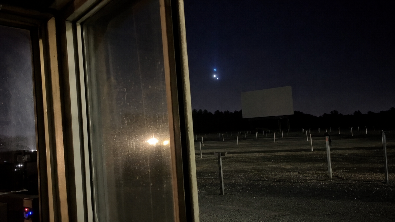 Phone video view from a projection booth doorway showing an unidentified light over the empty drive-in lot.