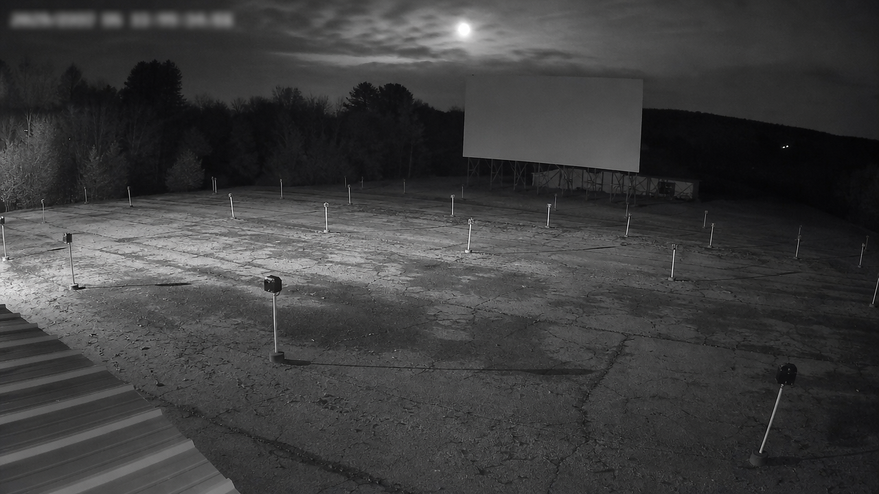 Security camera angle over cracked drive-in asphalt with an oval object above the old screen.