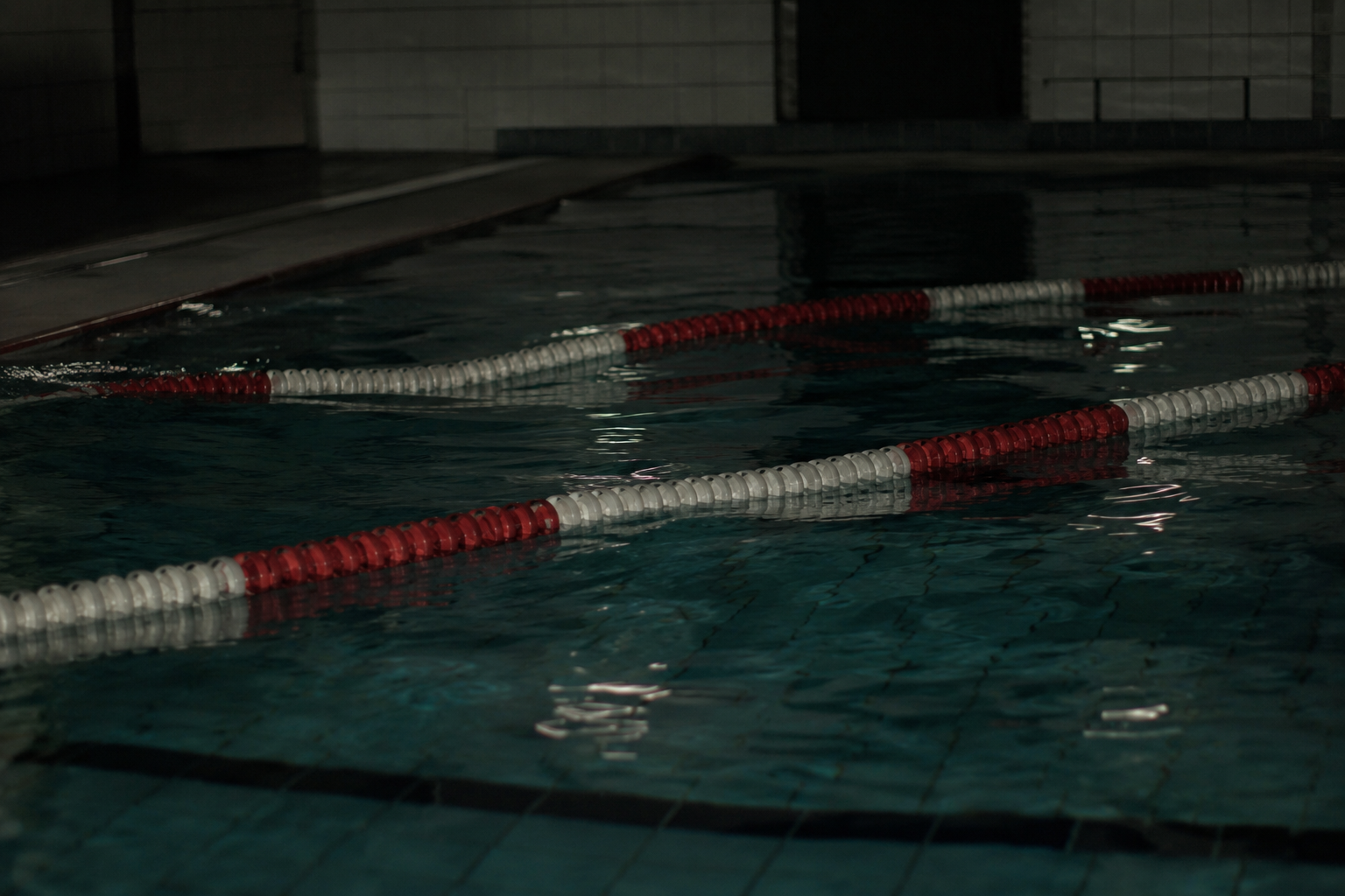 Lane ropes in a closed indoor pool appear to shift across rippling water after hours.