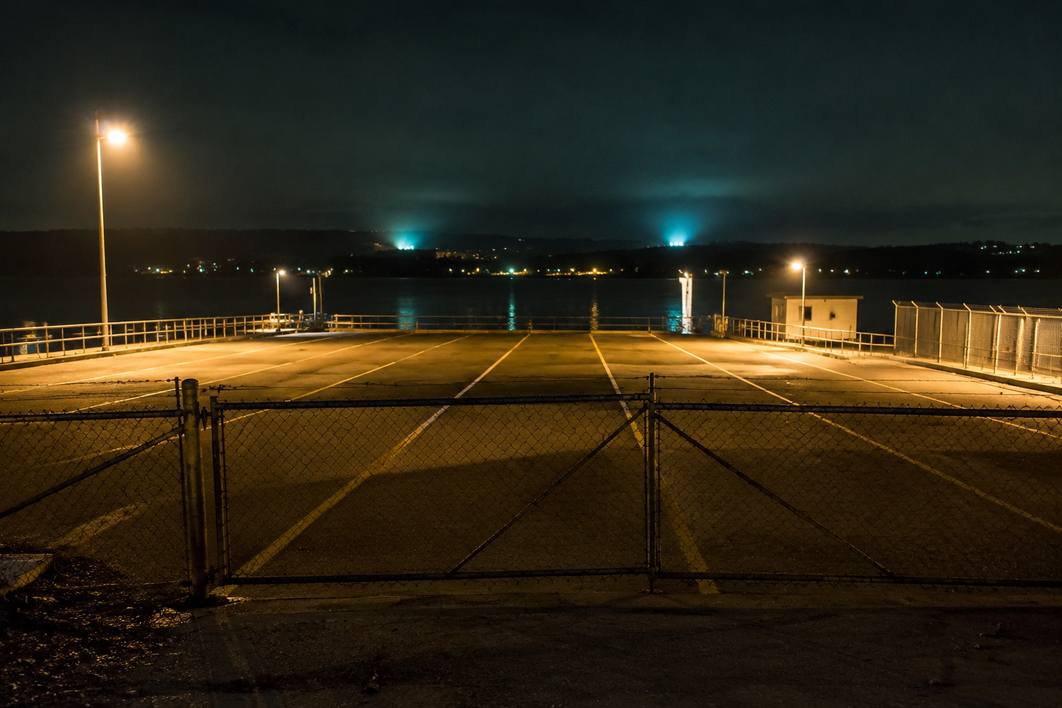 Empty ferry lot at night with unexplained lights over the water.