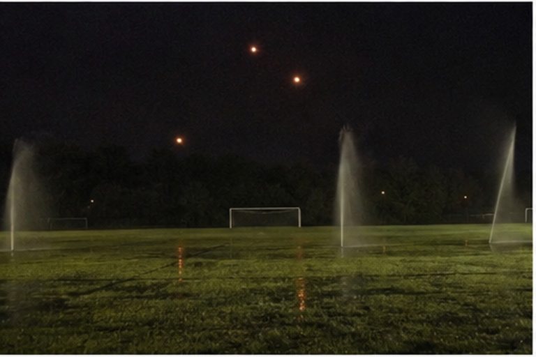 Three orange lights over an empty soccer field at night