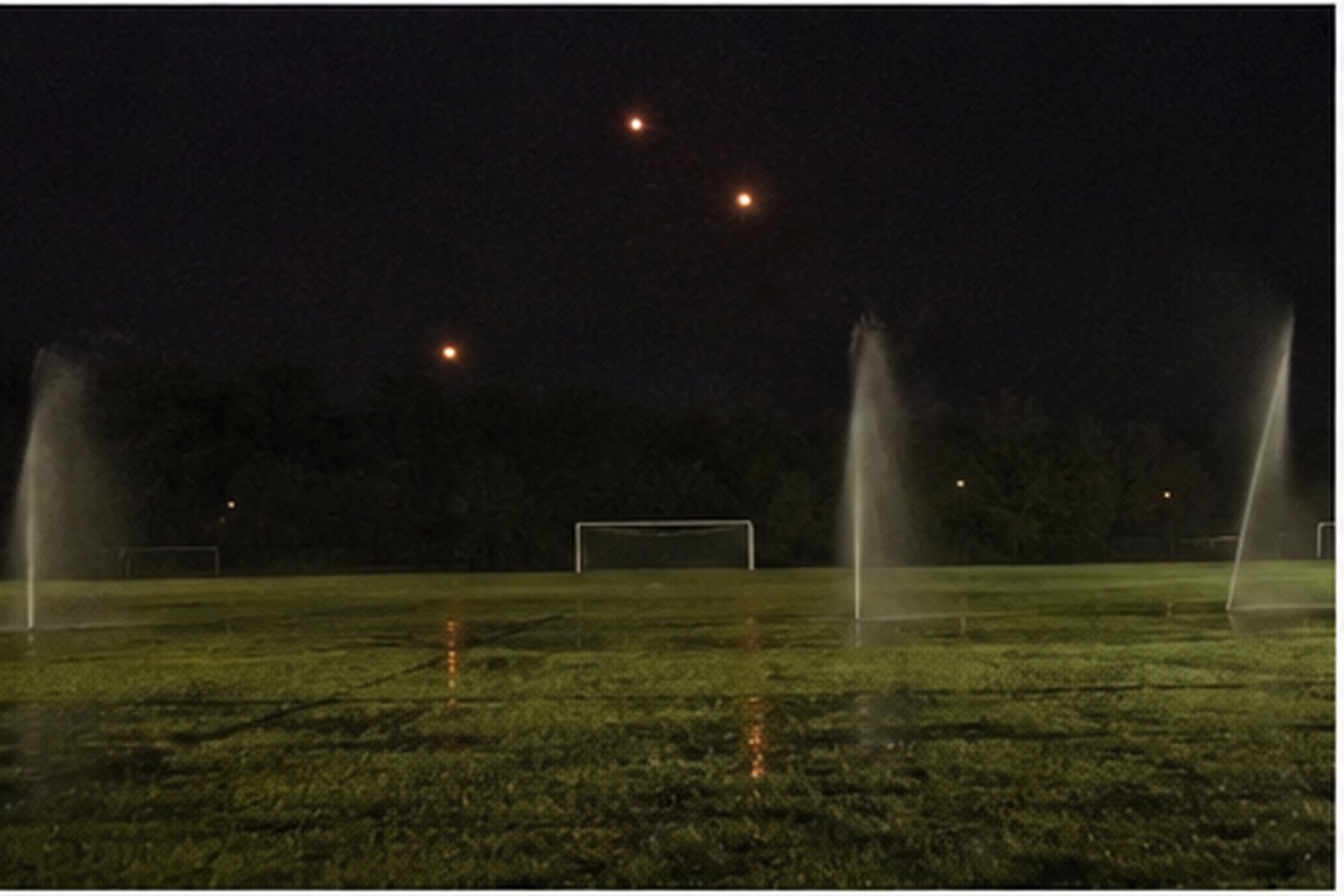 Three orange lights over an empty soccer field at night