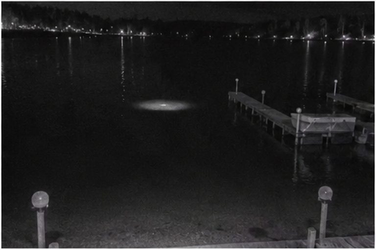 Pale disc reflection on dark lake water by a dock