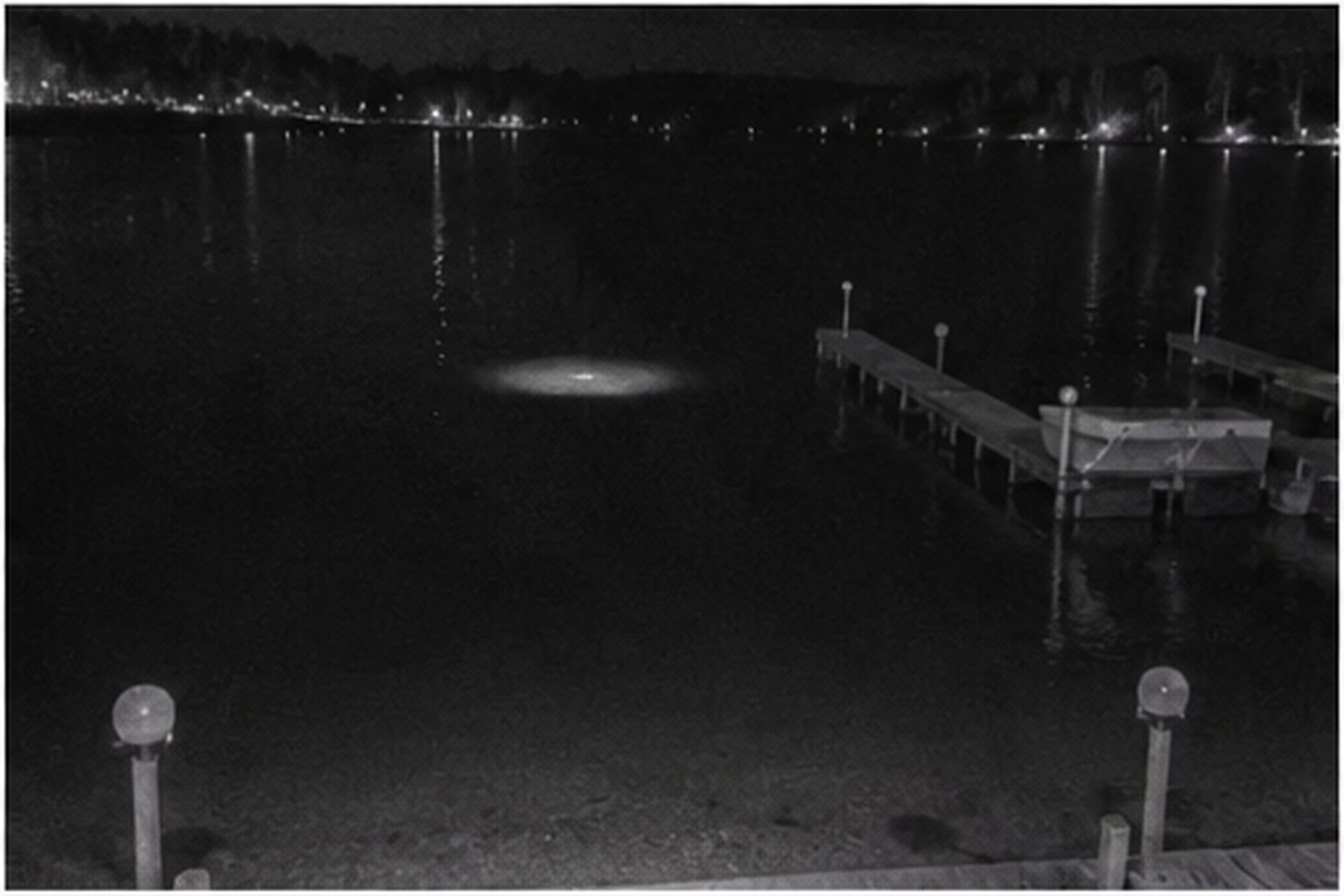 Pale disc reflection on dark lake water by a dock