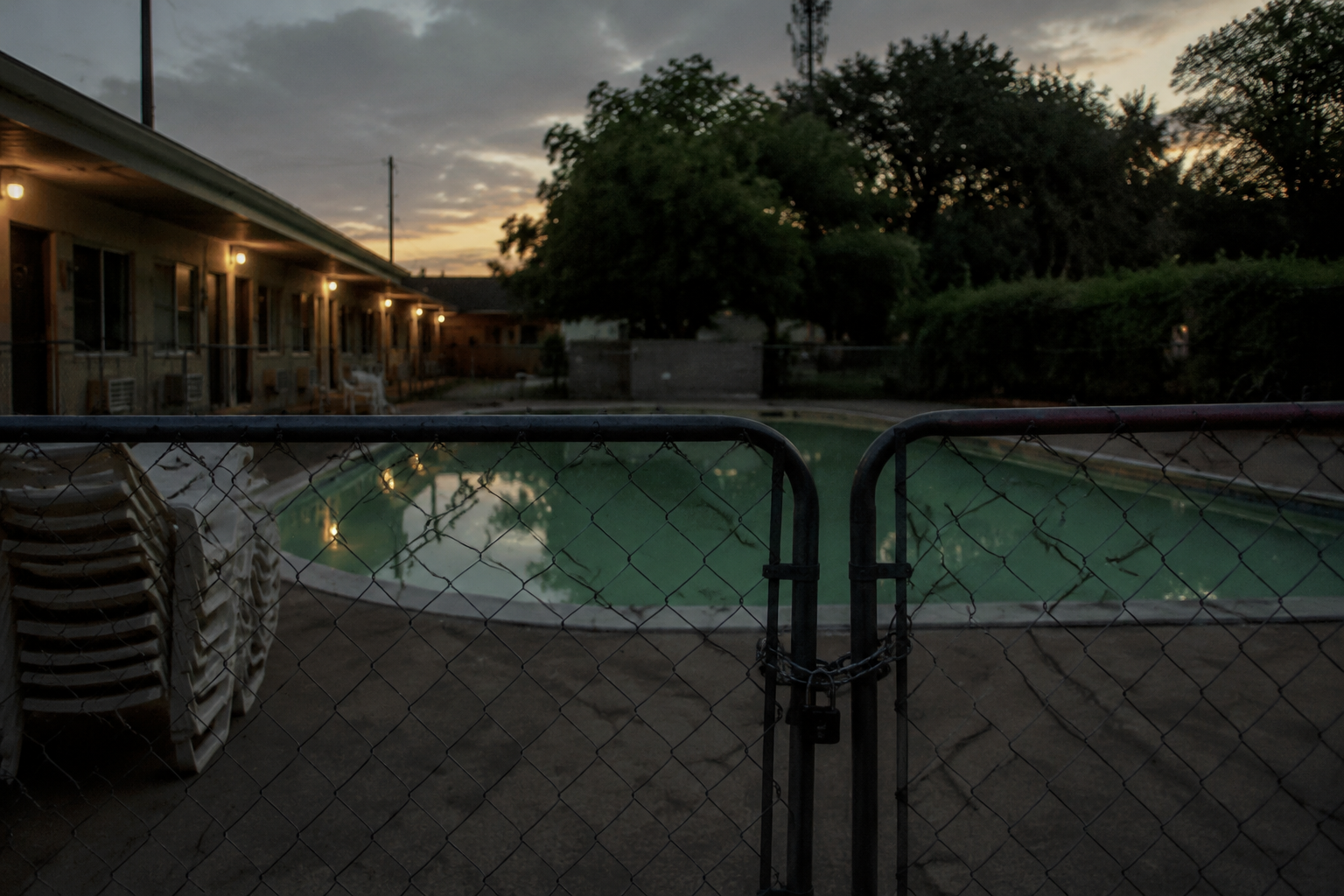 Locked motel pool area at dusk with still water and stacked chairs