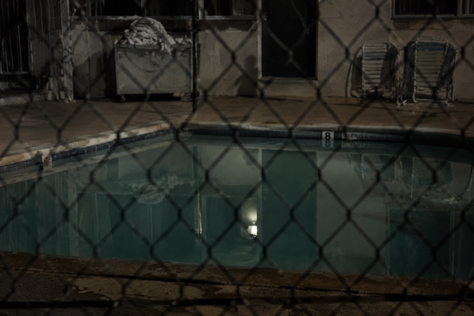 View through locked pool fence toward a faint shadow near the deep end