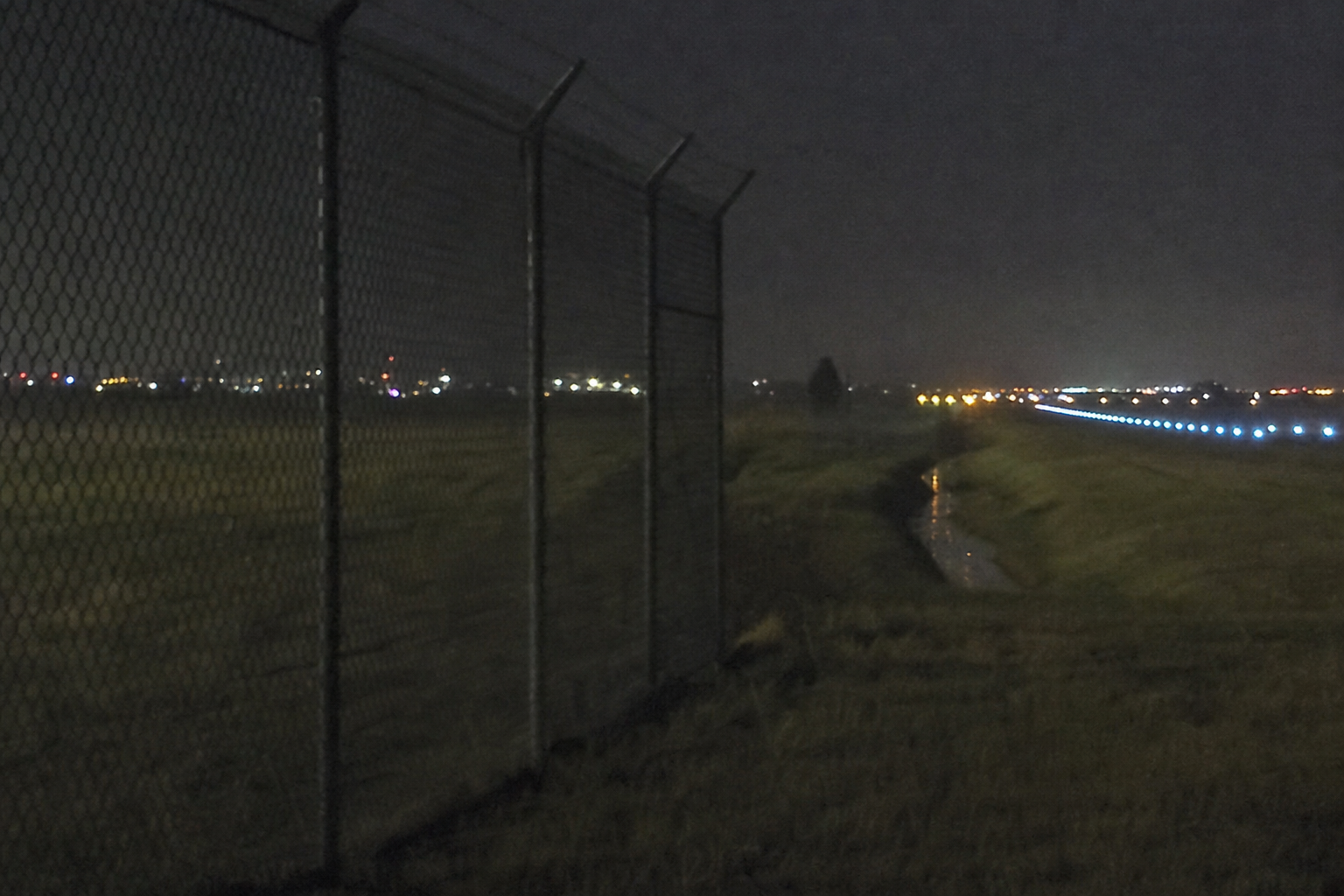 Security camera view of a broad dark figure beyond runway drainage lights