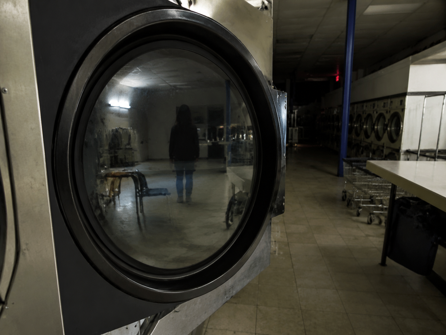 Dark figure reflected in laundromat dryer door