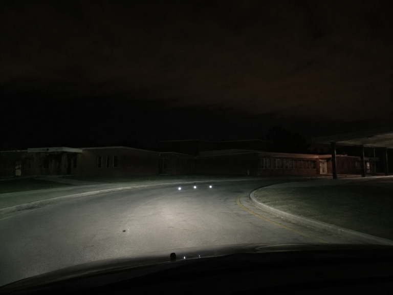 Three low lights hover over an empty rural school bus loop at night.