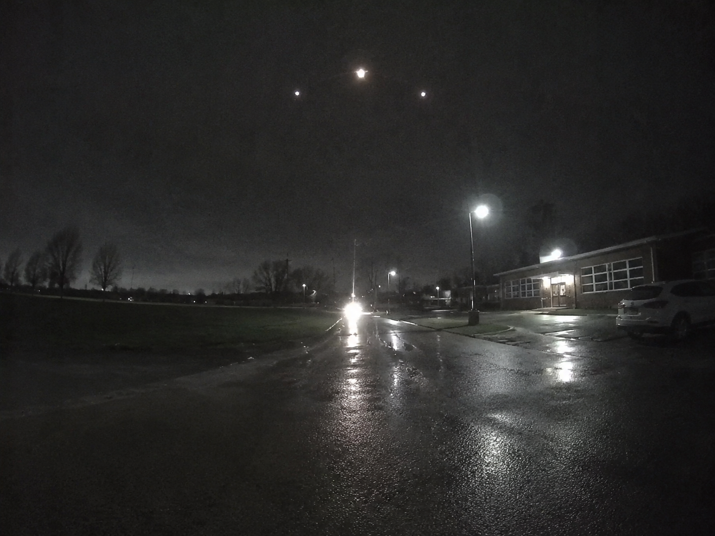 Three faint lights form a shallow triangle above wet school pavement.
