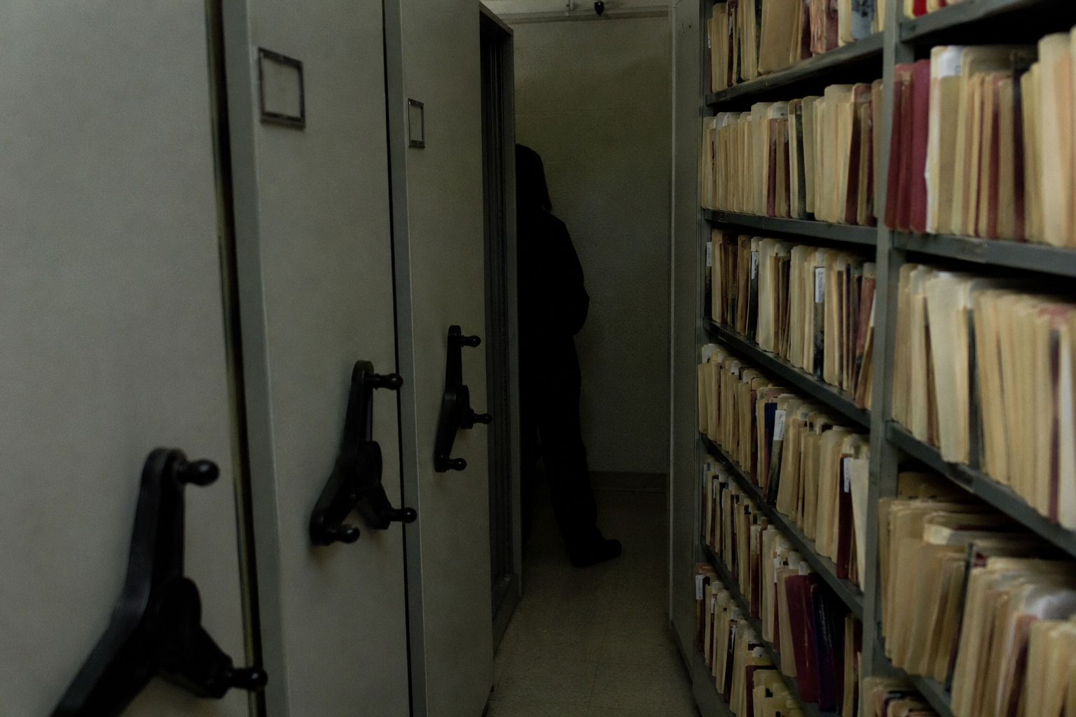 Dark figure partly hidden behind archive shelves