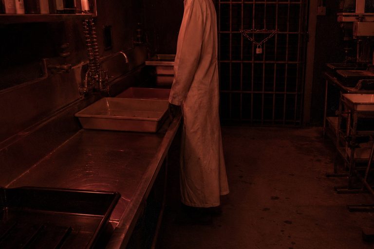 Editorial recreation of the Old Photo Lab Darkroom Camera Showed A White Apron Figure Standing Beside The Developing Sink story, image 1.