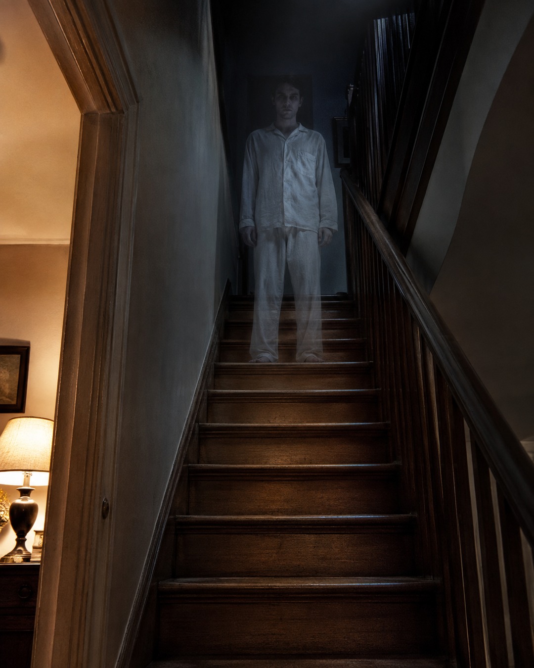 Editorial illustration of a pale apparition standing halfway up a dark home staircase.