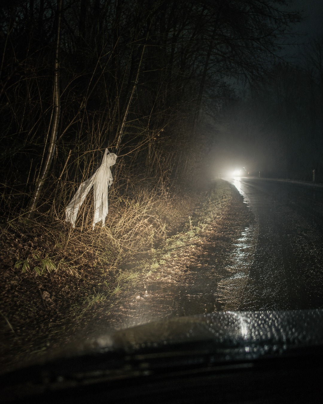 Editorial illustration of reflective roadside fabric and mist in headlights, showing how ordinary objects can resemble a figure.